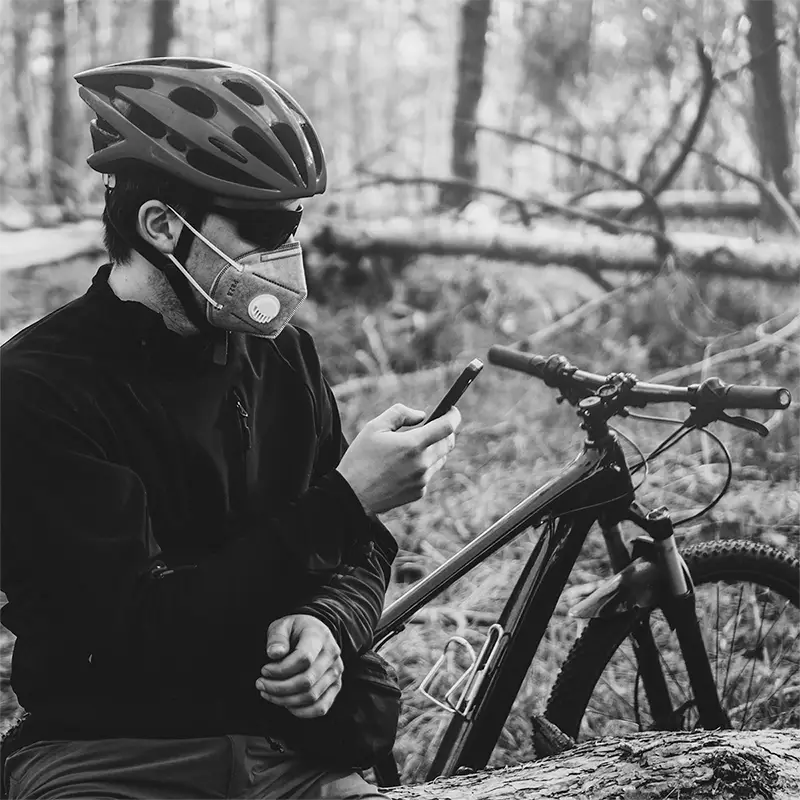 A person wearing a mask while out riding his bike, checks his phone.