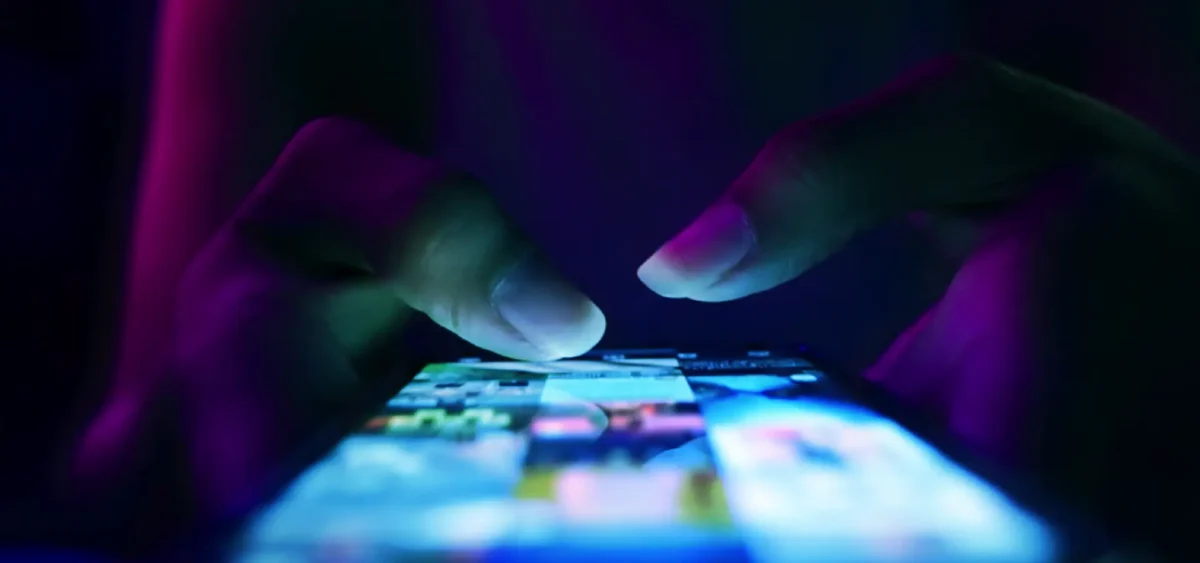 A person using their smart phone illuminated in the dark.