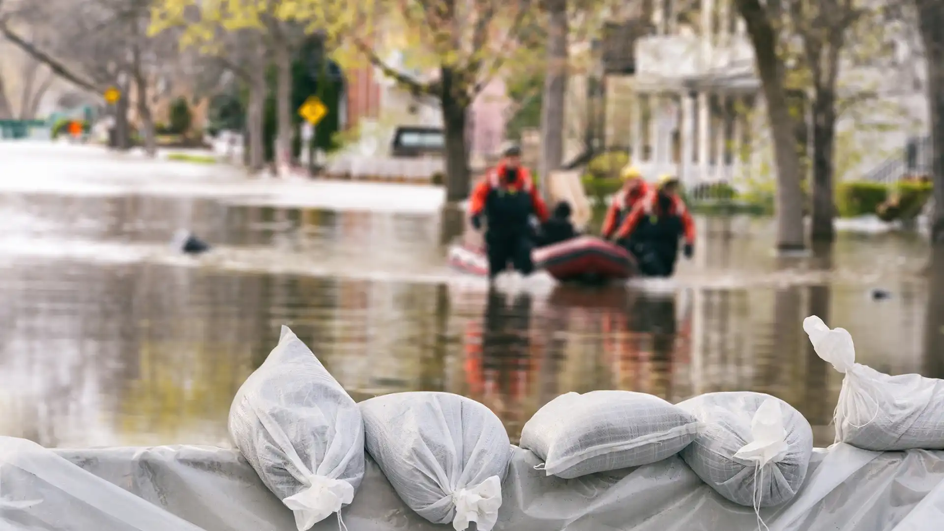 Sandbags stacked in front of a flooded neighborhood as rescue workers in a boat assist residents.