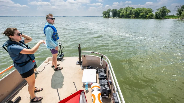 Two people standing on the end of a pontoon boat looking at a lake.