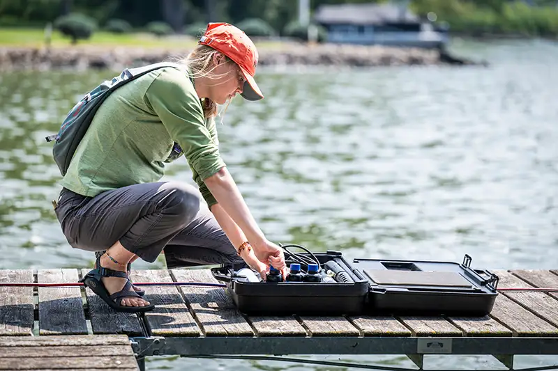 A student crouching on the end of a pier checking field research equipment.