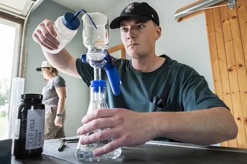 A student carefully transferring a water sample from a plastic squeeze bottle into a beaker.