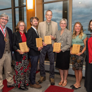 Dean Paul Robbins and Emily Reynolds, director of community engagement and alumni relations, pose with the alumni award winners. L-R: Robbins, Patricia O’Kane, Keefe Keeley, Robert Ribe, Margaret Krome, Breana Nehls, and Reynolds. (Not pictured is Distinguished Alumni Award winner Ashok Sarkar.) Photo credit: Ingrid Laas