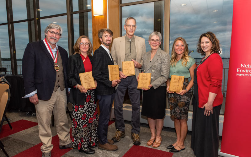 Dean Paul Robbins and Emily Reynolds, director of community engagement and alumni relations, pose with the alumni award winners. L-R: Robbins, Patricia O’Kane, Keefe Keeley, Robert Ribe, Margaret Krome, Breana Nehls, and Reynolds. (Not pictured is Distinguished Alumni Award winner Ashok Sarkar.) Photo credit: Ingrid Laas