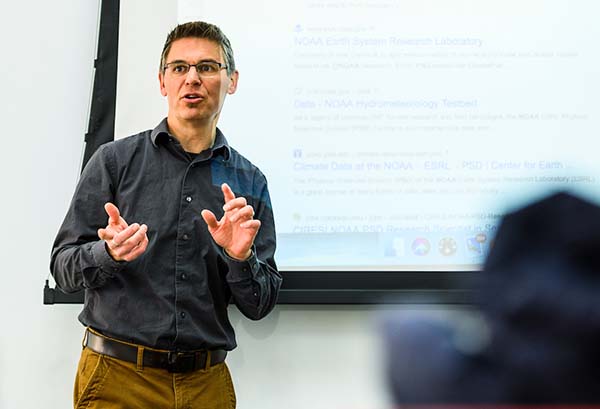Paul Block giving a classroom lecture in front of a screen showing a PowerPoint presentation