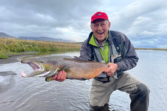 Steve Born dressed in waders and standing in stream holding a large rainbow trout
