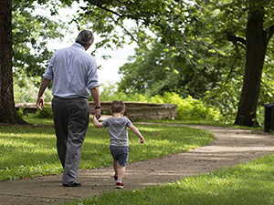 A father and young son holding hands and walking along a path in a park