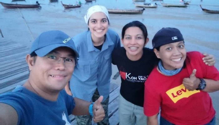 Group photo of four students posing next to a lake, with canoes in the background