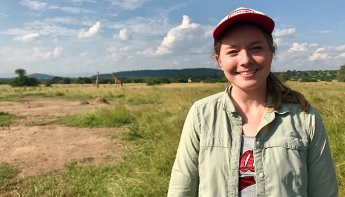 A student standing in an African prairie, with giraffes in the background