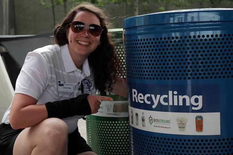 A student crouching next to a recycling container