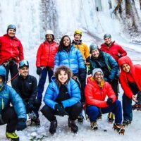 A diverse group of ice climbers posing in front of a frozen waterfall