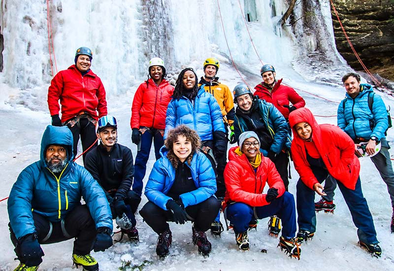 A diverse group of ice climbers posing in front of a frozen waterfall