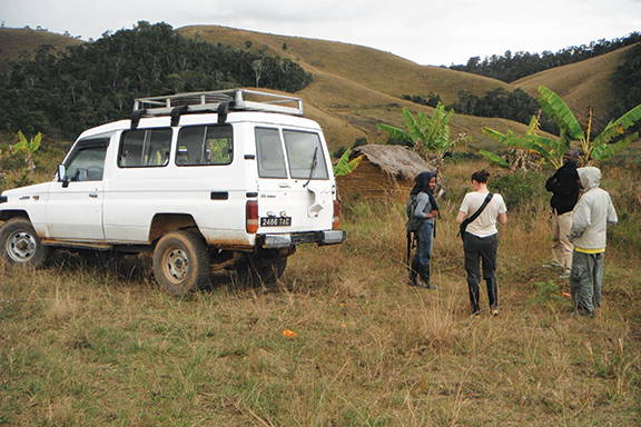 A sport-utility vehicle and a group of people in the foreground, with hilly terrain in the background
