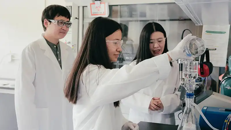 Researchers in a lab pouring water from a beaker into testing equipment.