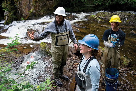 Three people in hard hats and waders discussing stream management