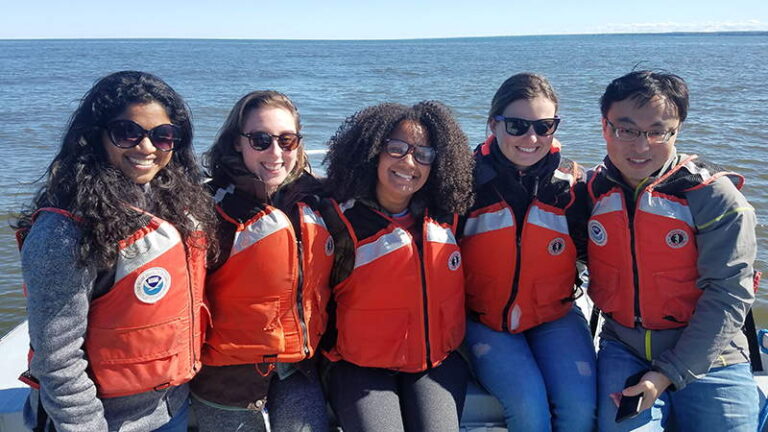 Five students wearing life jackets near a lake