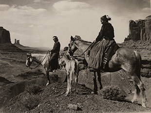Sepia-toned photo of two Native Americans riding horseback in a desert
