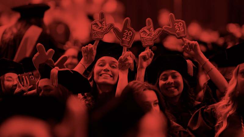 UW-Madison students at a graduation ceremony holding up small foam mitts to make a "W" sign.