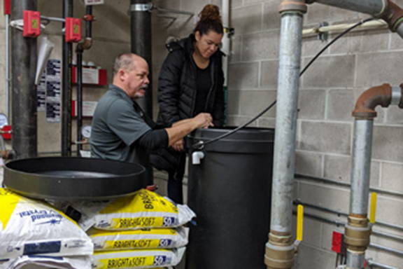 Two people looking into a water softener brine tank