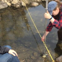 Two students test water and take measurements in a stream